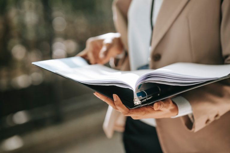 A person holding and reviewing a binder filled with documents, representing a professional setting where detailed document analysis or financial crime investigation is taking place.
